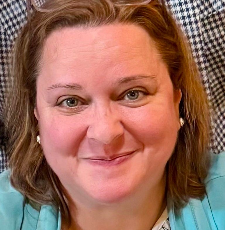 A picture of an adult white female, with auburn hair in a bob and a smirk on her face.